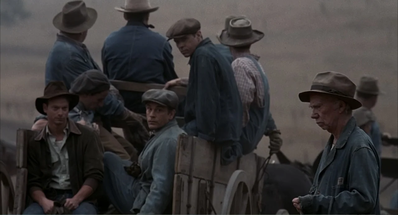 Of Mice and Men (1992) movie still: medium — A group of men sit on a wooden wagon traveling through a desolate field. They wear period-appropriate…