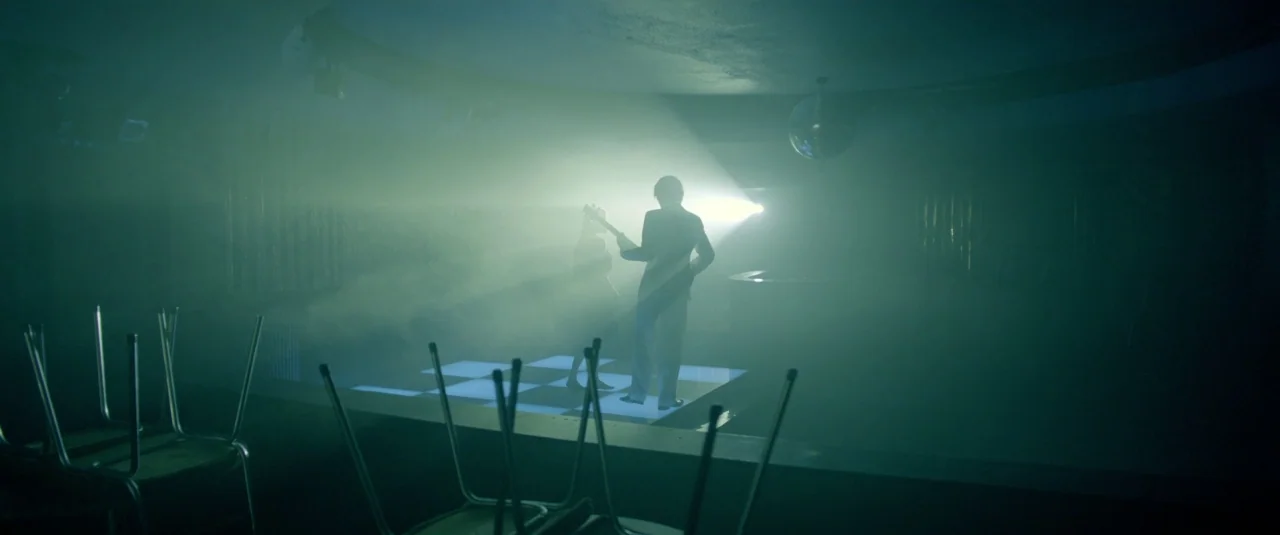 The Lure (2015) movie still: wide — A dark empty nightclub features a small, raised checkerboard dance floor in the center. Two figures stand on the…