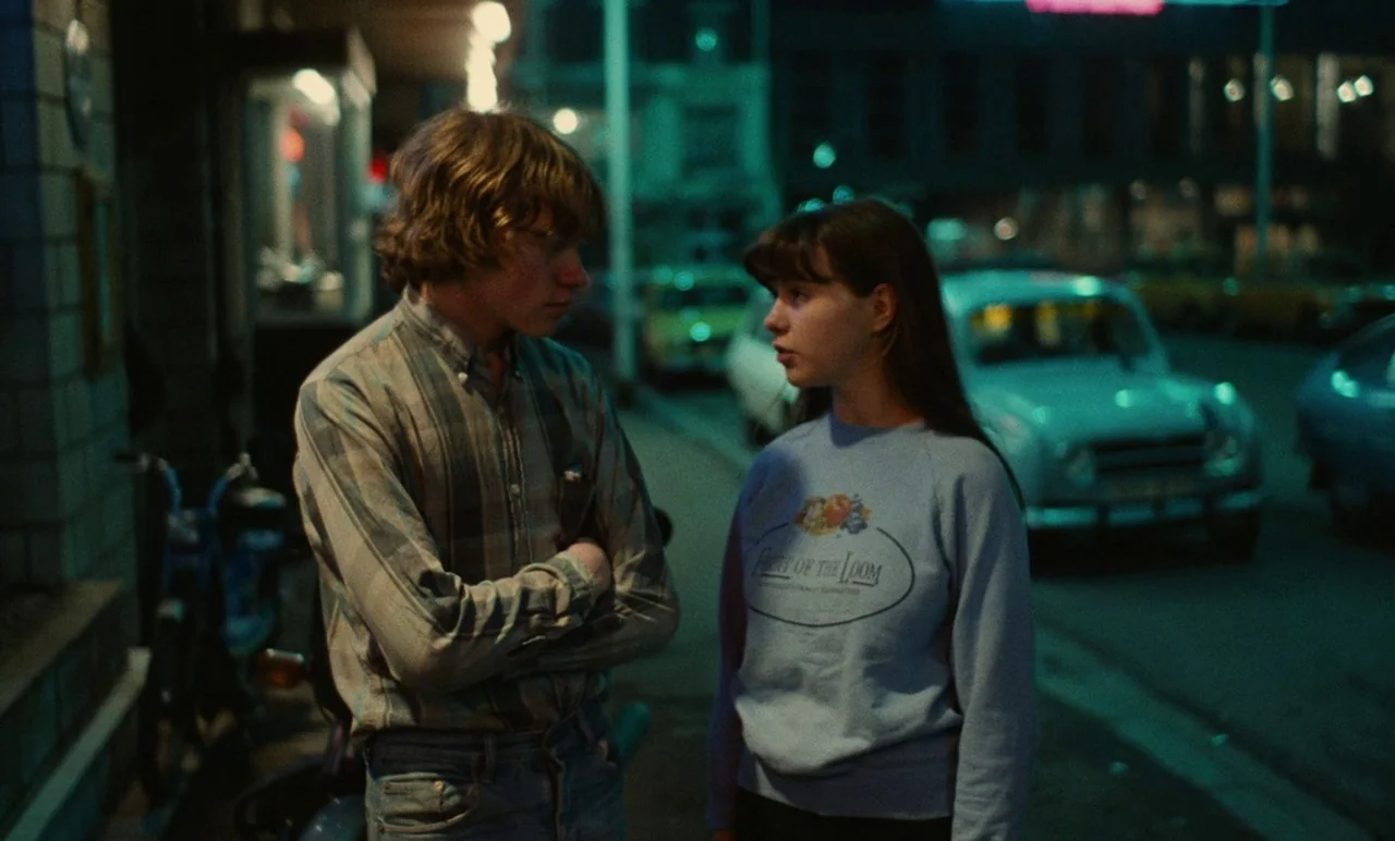 Graduate First (1978) movie still: medium — A man and woman talk on a dark urban sidewalk at night. A parked vintage car and a bicycle are visible…