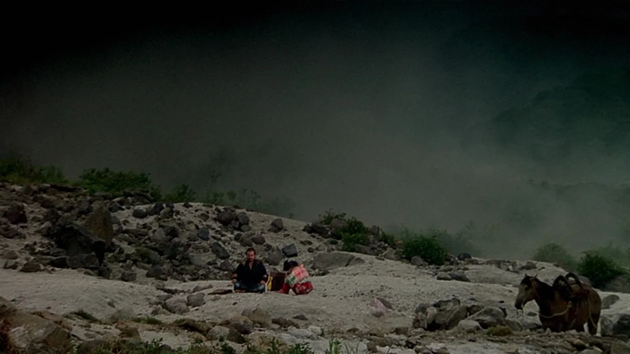 Ran (1985) movie still: wide — A vast, rocky, desolate landscape is shrouded in thick, low-hanging mist. Two figures sit together on the…