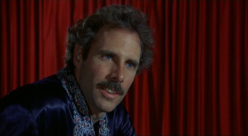 The King Of Marvin Gardens movie still: closeup — A man is positioned in front of heavy, vertically pleated red velvet curtains. He looks to his…