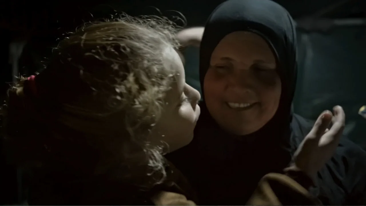 No Other Land (2024) movie still: closeup — A dimly lit interior space with shadows obscuring the surroundings. An elderly woman in a black hijab is…