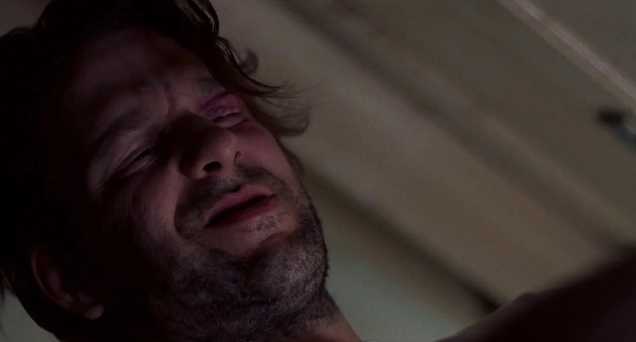 Barfly (1987) movie still: closeup — A man's face is seen from a low angle in a dimly lit, nondescript room. He lies still with his eyes partially…