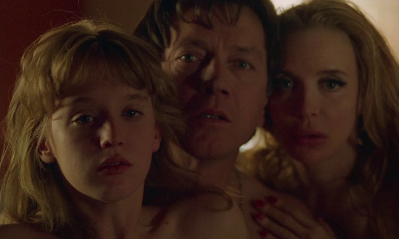 Water Drops on Burning Rocks (2000) movie still: closeup — A dimly lit indoor space features three people huddled together in close proximity. A man…