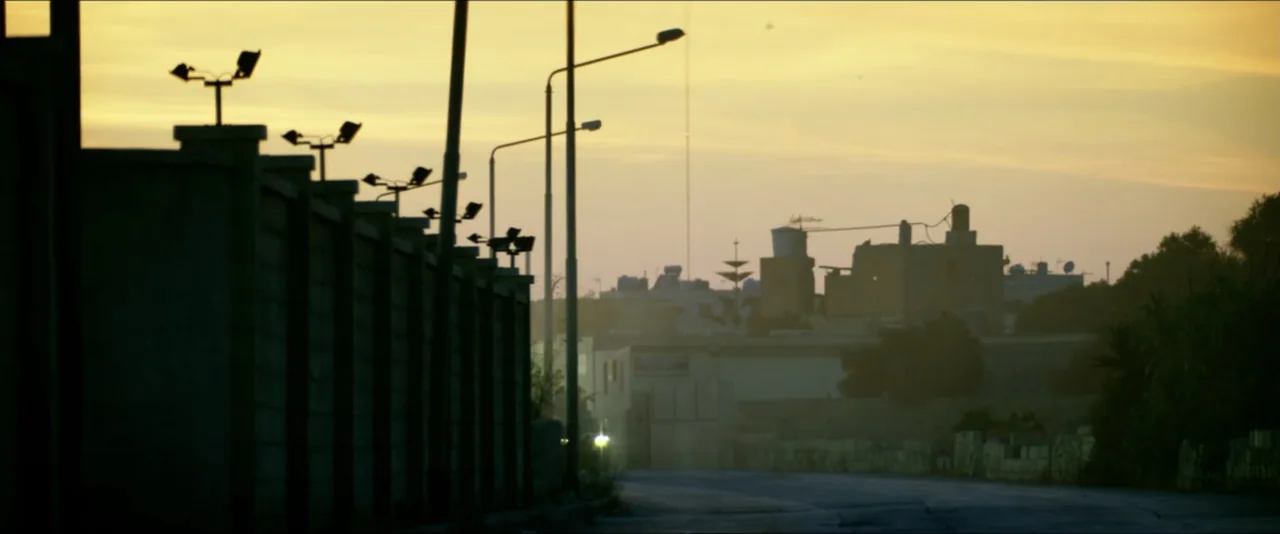 13 Hours: The Secret Soldiers of Benghazi (2016) movie still: establishing — An empty road runs past a concrete perimeter wall under a golden sky.…