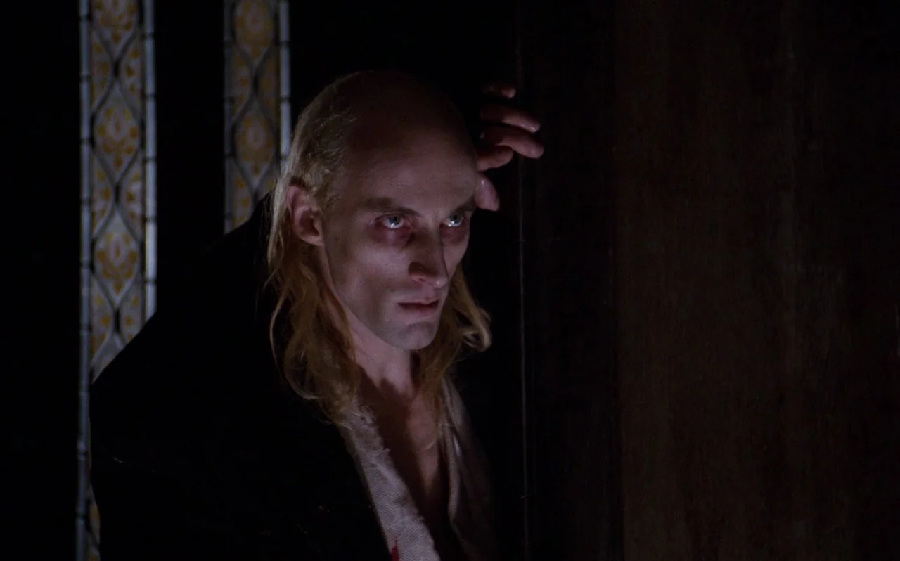 The Rocky Horror Picture Show (1975) movie still: medium — A dark corridor features a stained glass accent panel beside a vertical wooden frame. A…