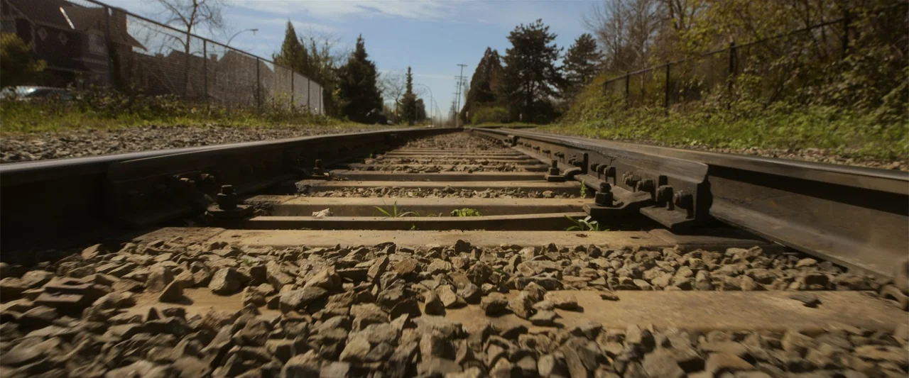 Final Destination Bloodlines (2025) movie still: establishing — Low angle view along a set of railway tracks stretching toward the horizon line. The…