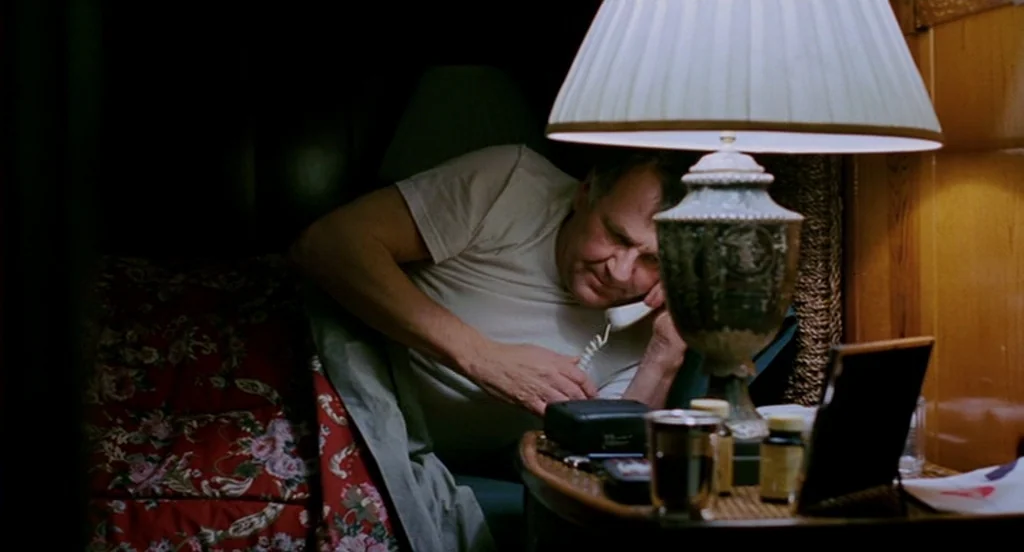 Eternal Sunshine of the Spotless Mind (2004) movie still: medium — A man lies in bed at night with a red floral patterned quilt. He holds a white…