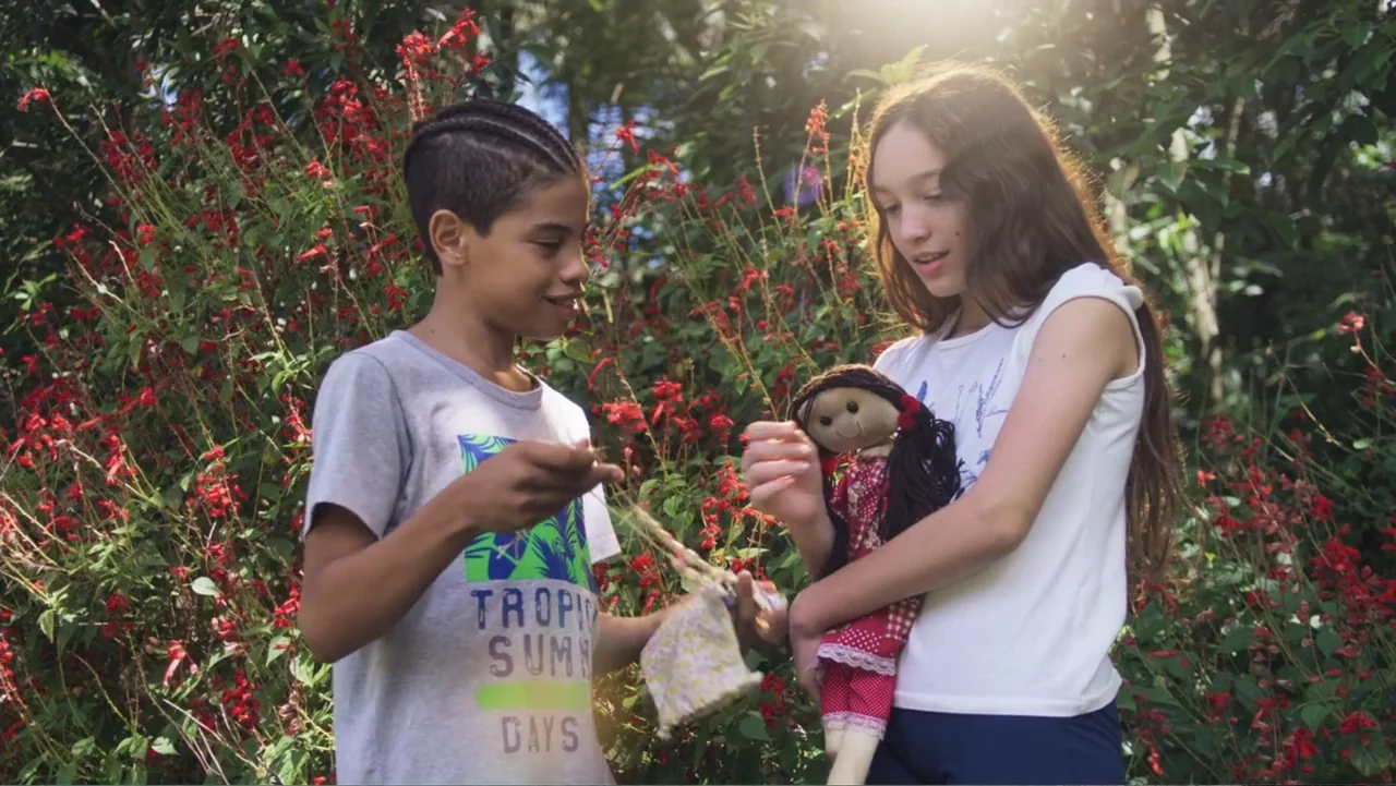 Making of: Scars of Beauty (2025) movie still: medium — A pair of children interact near a dense cluster of blooming red flowers outdoors. The girl…