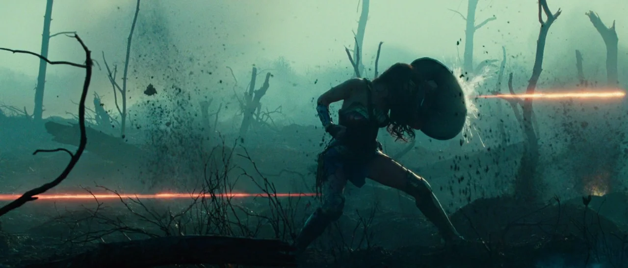 Wonder Woman (2017) movie still: wide — A desolate, war-torn landscape is filled with scorched trees, smoke, and debris. A woman in battle armor…