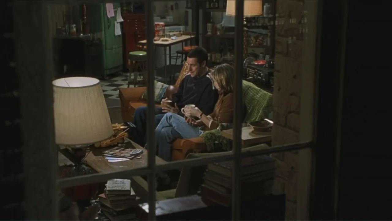 Big Daddy (1999) movie still: medium — A cluttered living room interior is viewed through a window grid at night. A man and a woman sit together on…