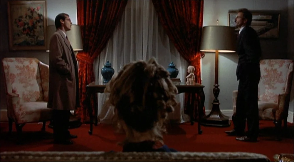 The King Of Marvin Gardens movie still: medium — A furnished interior features red curtains, patterned armchairs, and a central table with vases.…