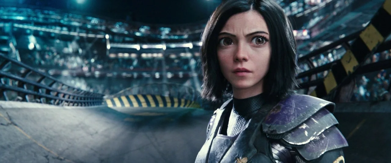 Alita: Battle Angel movie still: medium — A large, industrial sport arena features a smooth, banked curved track with yellow barriers. A young woman…