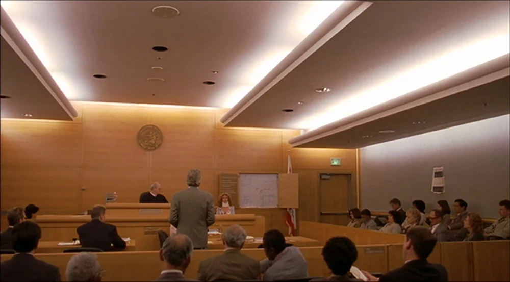 Erin Brockovich (2000) movie still: wide — A modern, wood-paneled courtroom features a judge at the bench and numerous attendees. A man in a suit…