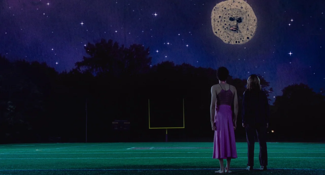 I Saw The TV Glow (2024) movie still: wide — A dark night at a football field under a sky filled with bright stars. Two young women stand on the…