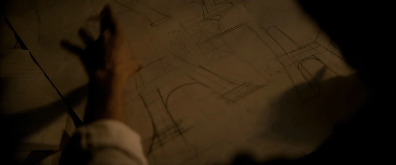 Eiffel (2021) movie still: closeup — A dark, wood-paneled room contains a large table covered with detailed architectural drawings. A person's hand…