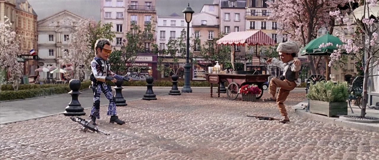Team America: World Police movie still: wide — A European-style cobblestone plaza features cherry trees and large black decorative chess pieces. Two…