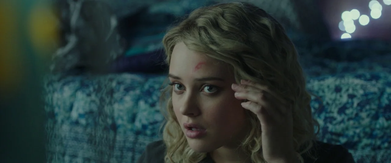 Spontaneous (2020) movie still: closeup — A dimly lit bedroom features a patterned blue bedspread and out-of-focus bokeh lights. A young woman with…