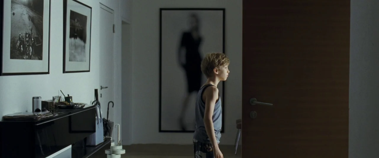 Goodnight Mommy (2014) movie still: medium — A modern hallway features white walls adorned with large black and white framed photography. A young…
