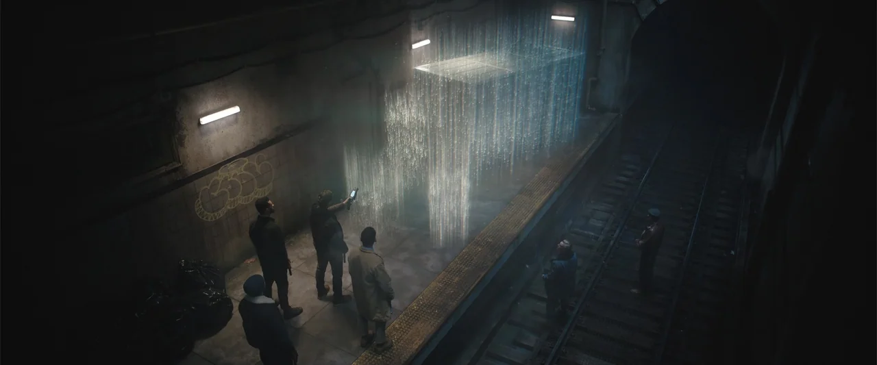 Play Dirty (2025) movie still: wide — A dimly lit subway platform with graffiti on the walls and dark train tracks below. A small group of people…