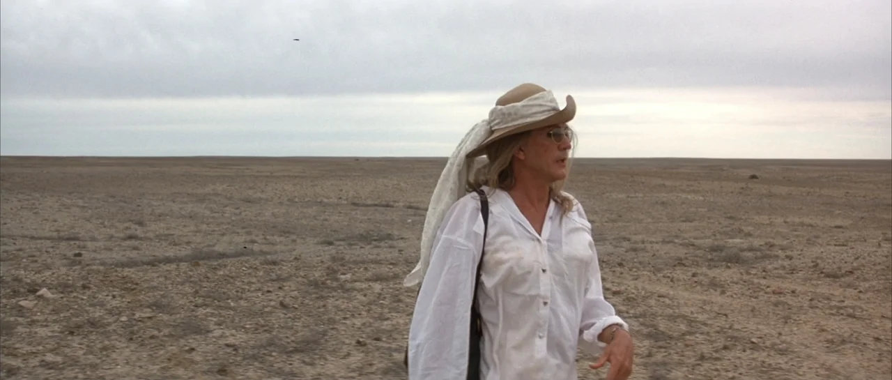 The Adventures of Priscilla, Queen of the Desert (1994) movie still: medium — A flat, dusty desert expanse stretches under a wide, overcast sky. A…