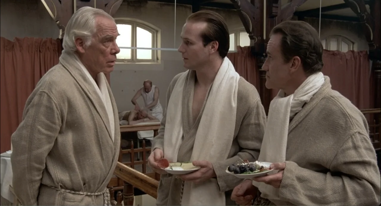 Gorky Park (1983) movie still: medium — An interior space with wooden roof beams, red curtains, and an arched window. Three men in beige robes stand…
