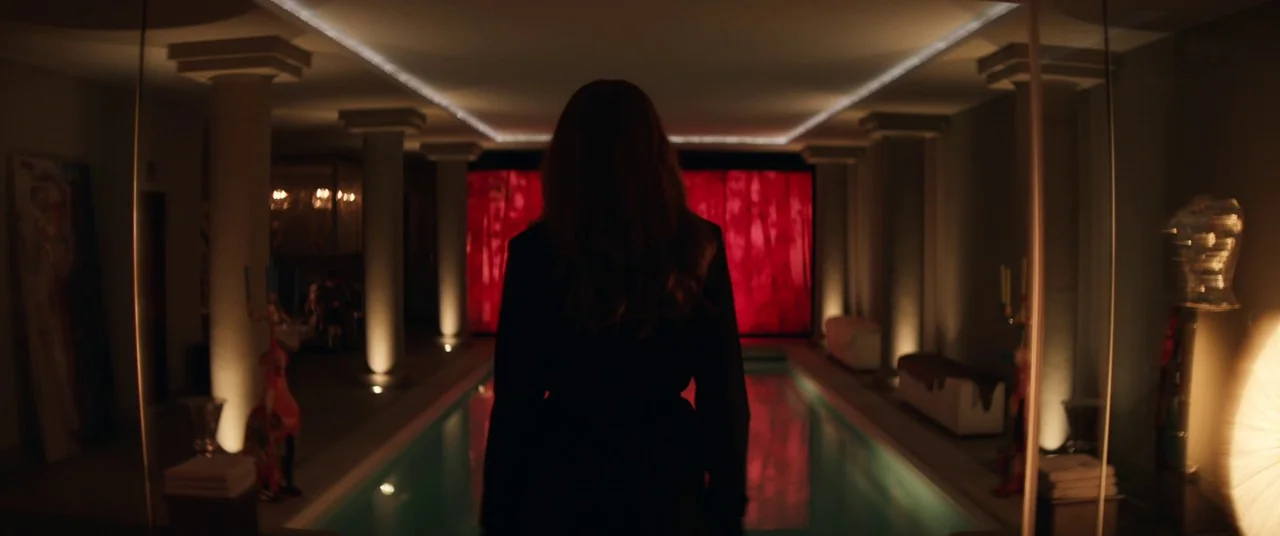 The Rhythm Section (2020) movie still: medium — An indoor pool area features neoclassical columns and a large glowing red screen background. A woman…