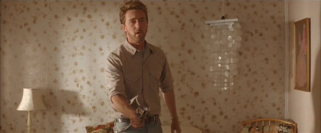 Down In The Valley (2005) movie still: medium — A motel room features walls covered in pale floral patterned wallpaper and shell decor. A man stands…