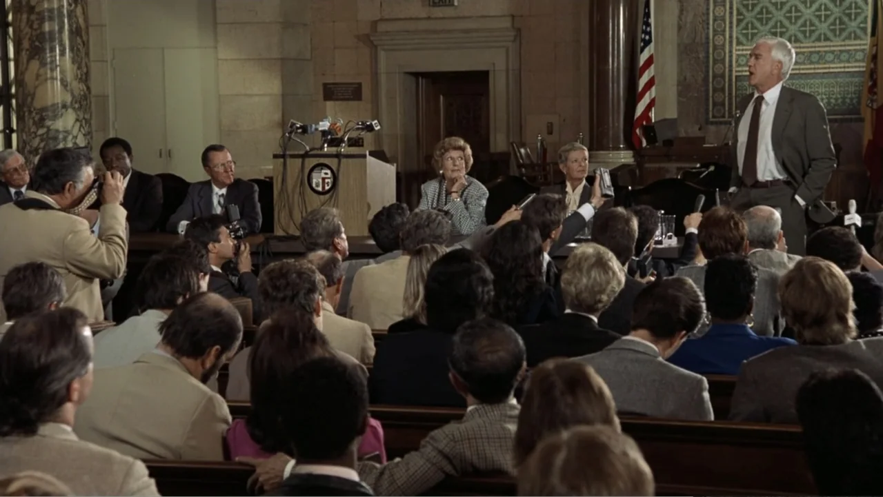 The Naked Gun: From the Files of Police Squad! (1988) movie still: medium — An interior courtroom with wooden benches, a raised podium, and an…