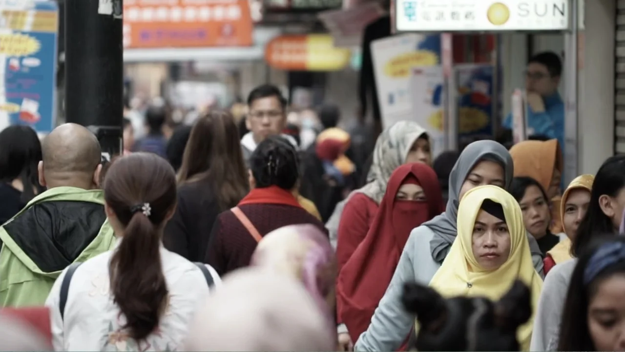 Escape From Saudi (2019) movie still: medium — A dense urban street features pedestrians walking past shopfronts with visible signage. Multiple…