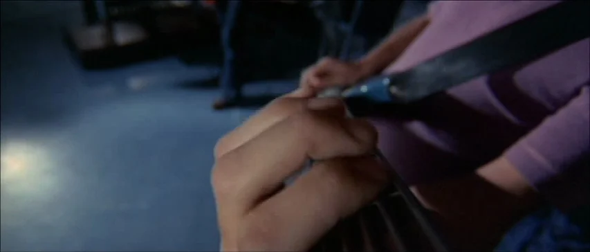 Four Flies On Grey Velvet (1971) movie still: closeup — A dimly lit rehearsal space features a musician practicing on a bass guitar. Close focus…