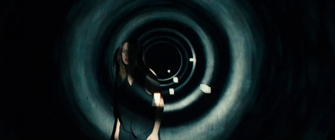 Silver Haze (2023) movie still: medium — A woman stands within the curved concrete walls of a large dark pipe. She remains still while positioned…