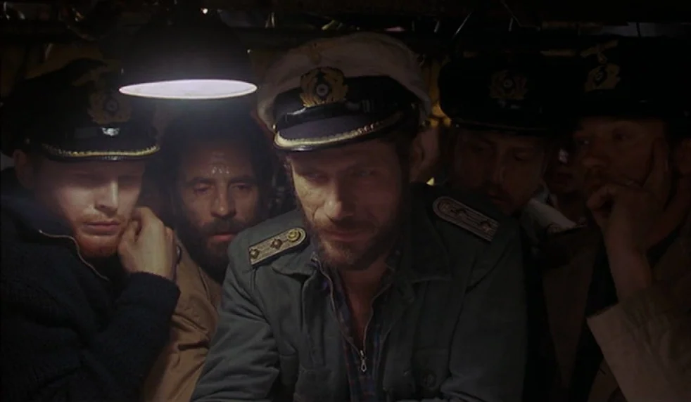 Das Boot (1981) movie still: medium — A cramped, dimly lit submarine compartment is packed with men in naval uniform. The men stand in close…