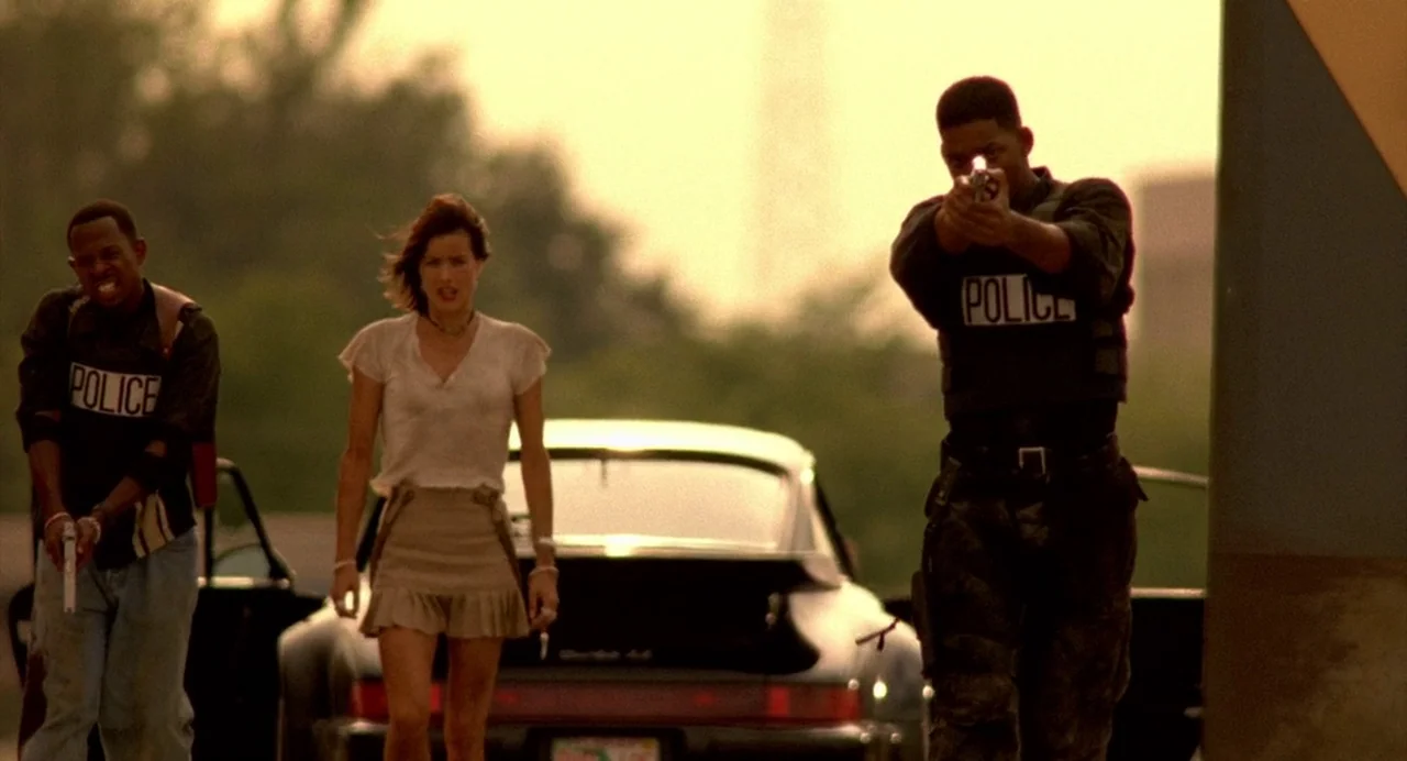 Bad Boys (1995) movie still: fullbody — Three individuals move toward the camera across a paved surface during golden hour. A black sports car is…