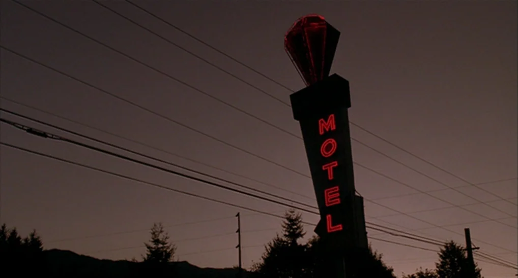 Twin Peaks: Fire Walk With Me (1992) movie still: establishing — A vertical neon sign stands against a darkening twilight sky with distant…