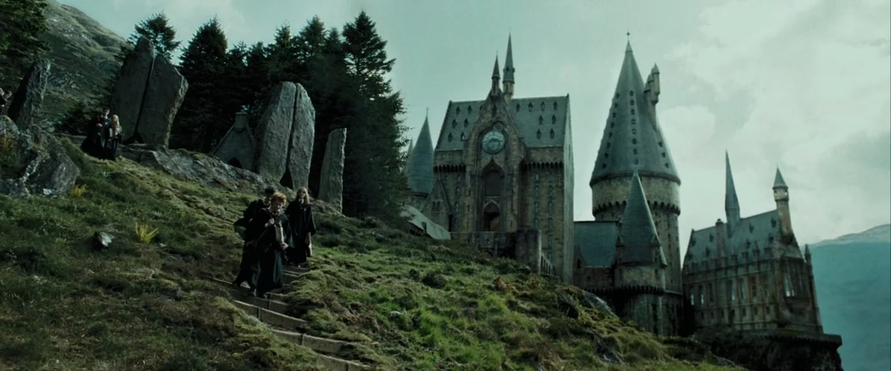 Harry Potter and the Prisoner of Azkaban (2004) movie still: wide — A stone castle with tall spires stands on a rocky cliff overlooking a lake.…