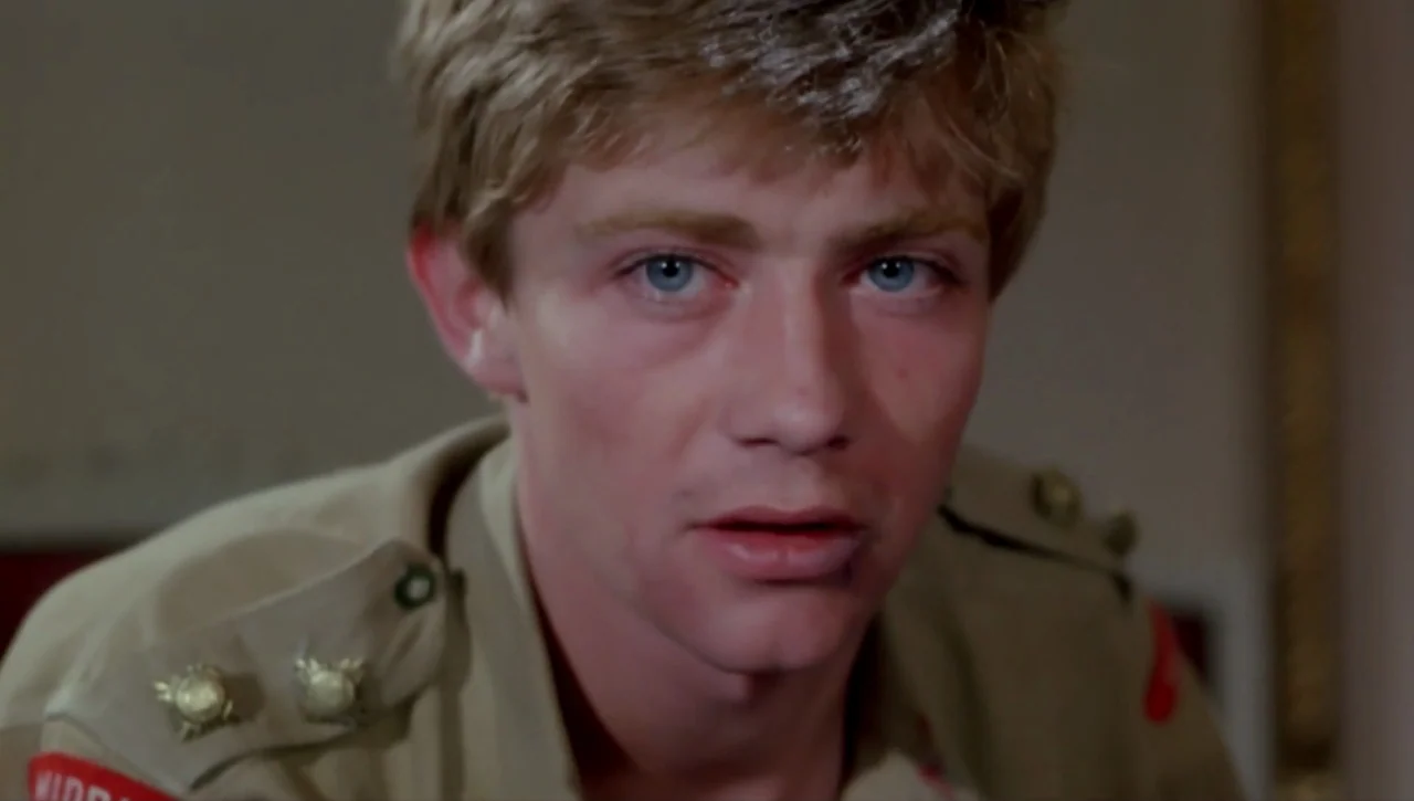 Alexandria…Why? (1979) movie still: closeup — An interior space with a neutral wall background. A young man wearing a tan military uniform looks…