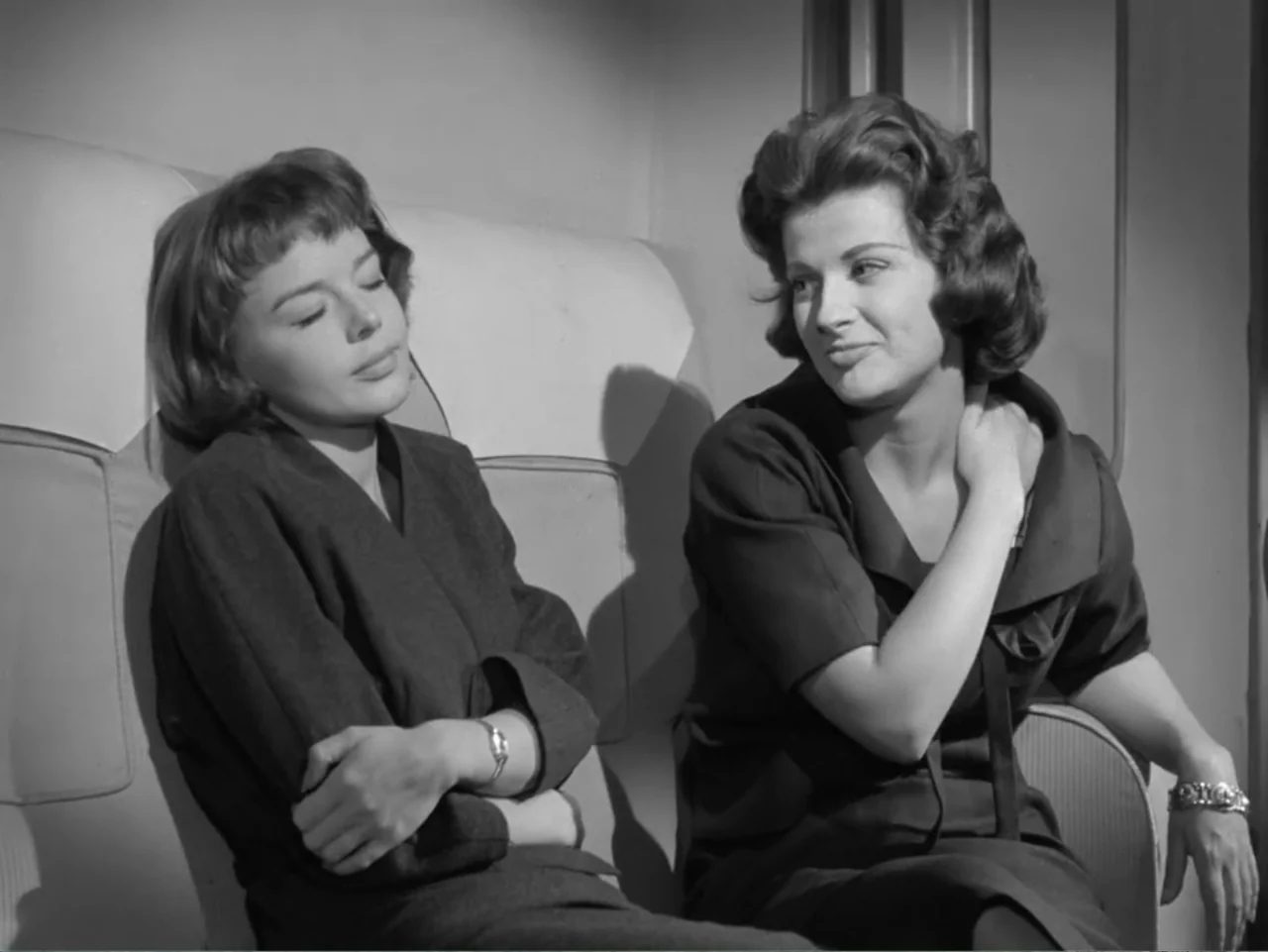 The Crawling Eye (1958) movie still: medium — Two women sit side by side in a narrow upholstered train compartment. One woman rests with her eyes…