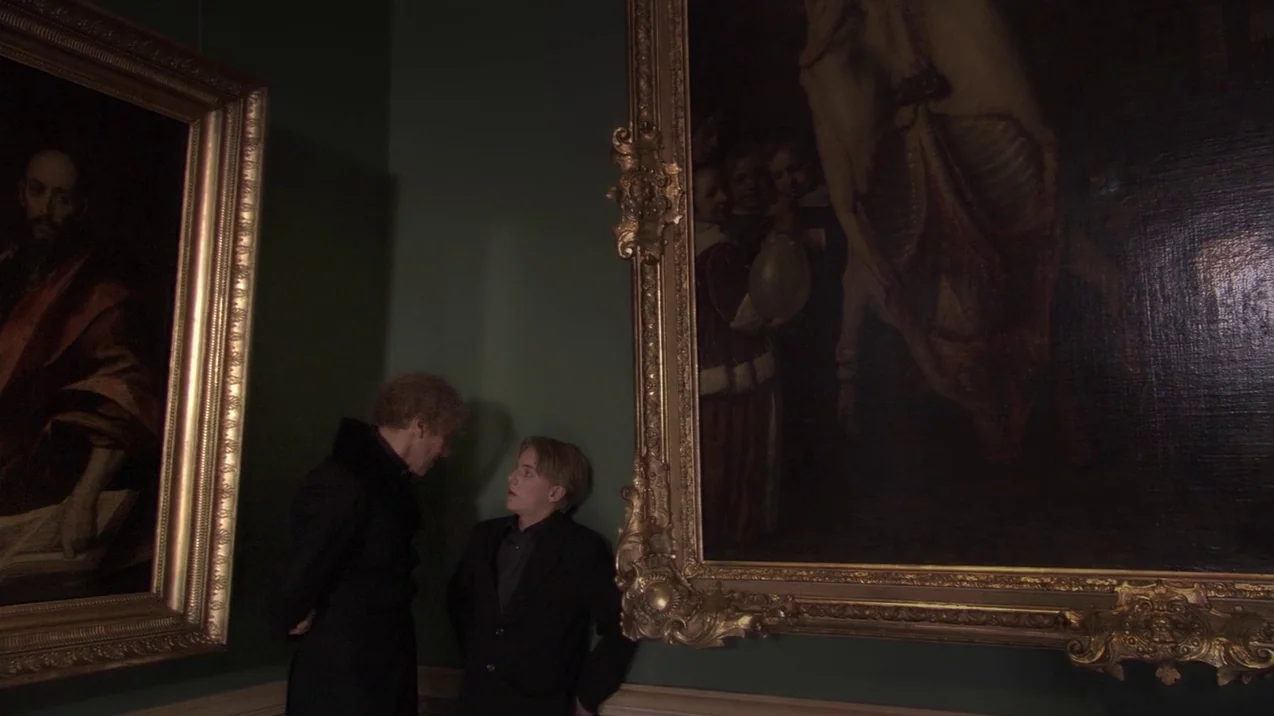 Russian Ark (2002) movie still: wide — An art gallery space features dark green walls decorated with large, ornate, gold-framed oil paintings. Two…