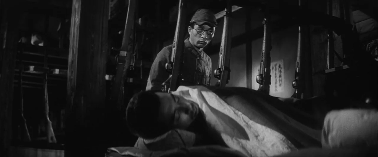 The Human Condition II: Road to Eternity (1959) movie still: medium — A dimly lit room filled with racks of rifles stored against wooden support…