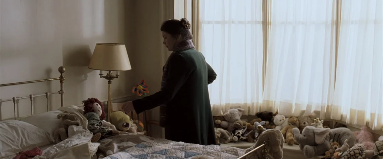 No Reservations (2007) movie still: medium — A light-colored nursery contains a single bed covered in numerous plush toys and dolls. A woman in a…
