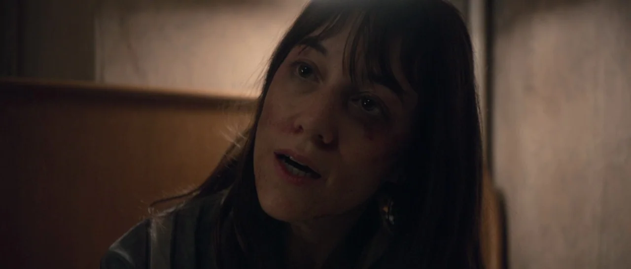 Nymphomaniac Vol 1 (2013) movie still: closeup — A dimly lit room features a woman with bruises near her eyes and cheeks. The woman looks toward…
