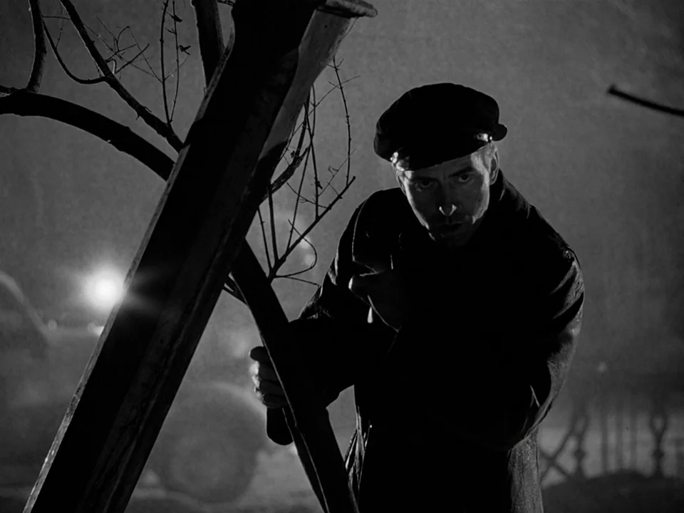 It’s A Wonderful Life (1946) movie still: medium — A dark urban setting at night features a man standing by a wooden post. The man watches the…