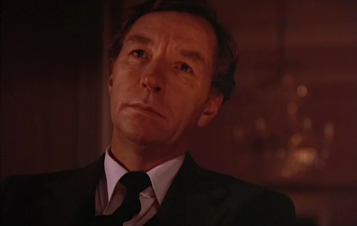 Autumn Sonata (1978) movie still: closeup — A dimly lit interior space features a man in a formal dark suit. He stares forward with an unreadable…