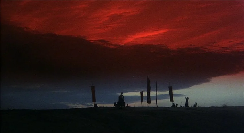 Kagemusha (1980) movie still: wide — A vast field under a dramatic dark red and grey sunset sky. A small group of silhouetted riders on horseback…