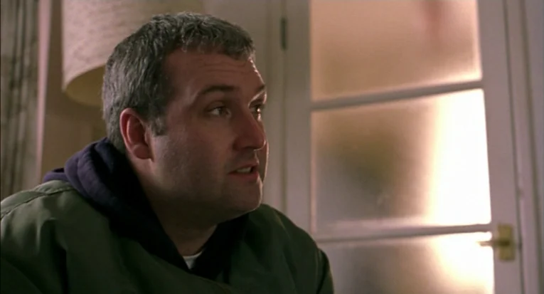 A Room For Romeo Brass (1999) movie still: closeup — An interior space features a white door with frosted glass panels in the background. A man in a…