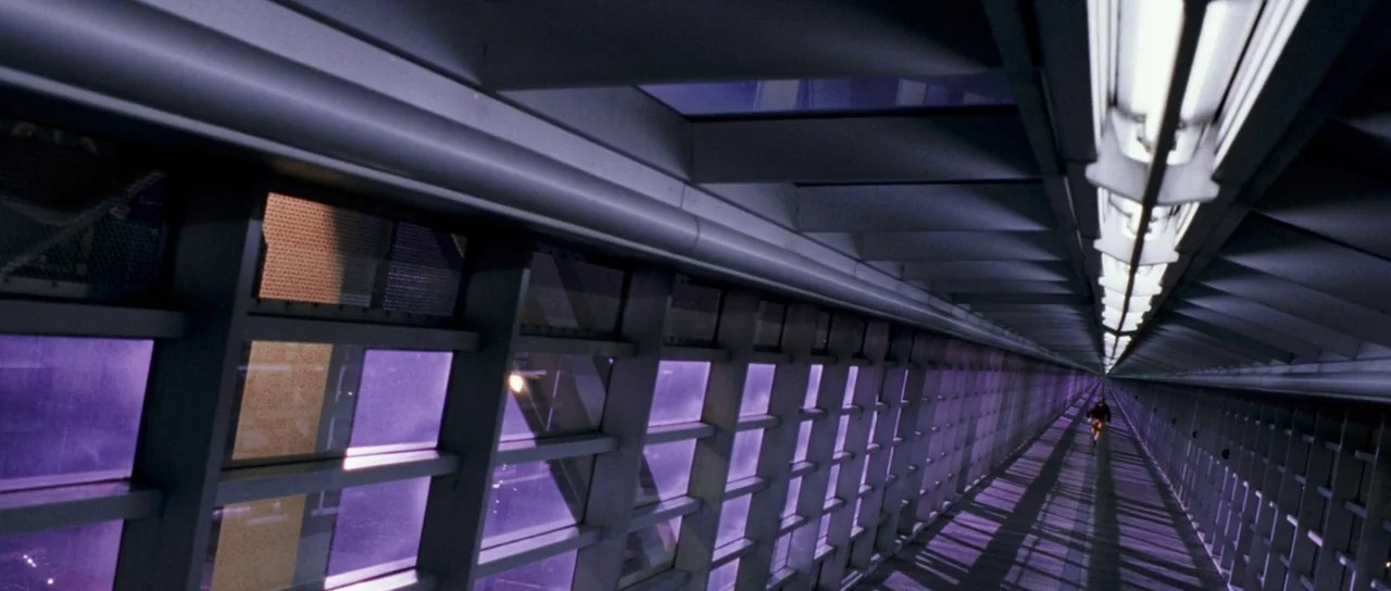 Stay (2005) movie still: wide — A long, enclosed pedestrian walkway features a repetitive grid structure and expansive purple-tinted glass. A single…