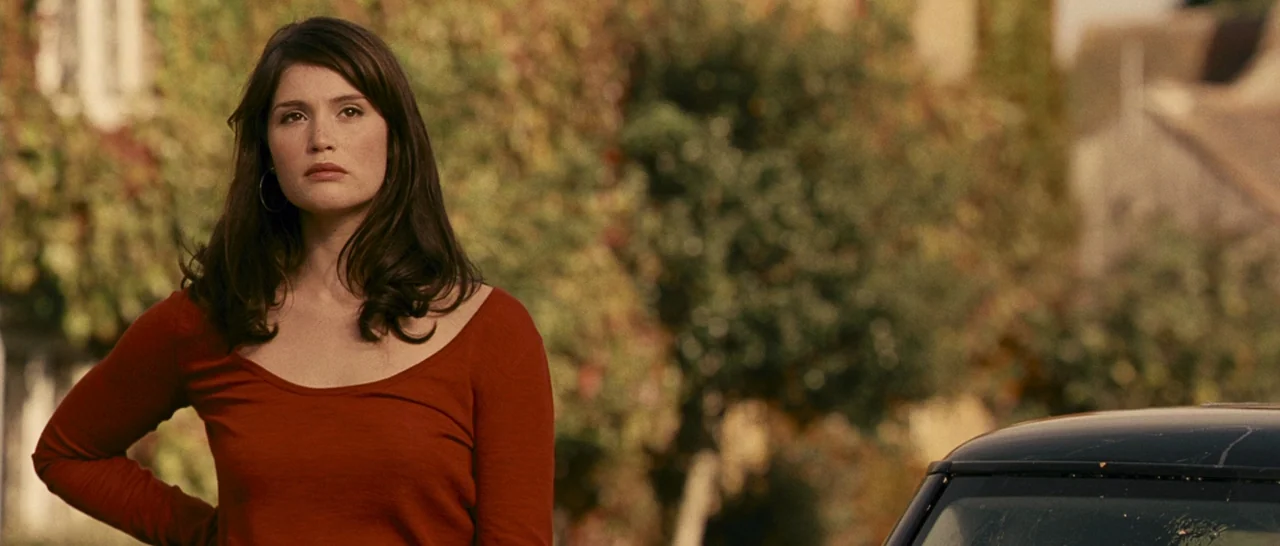 Tamara Drewe (2010) movie still: medium — An exterior street scene features a woman standing before blurred autumn foliage. She stands on the left,…