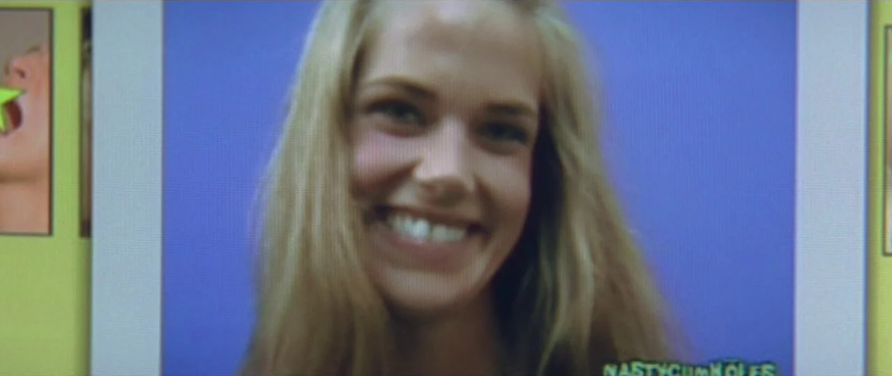 Afterschool (2008) movie still: closeup — A close-up of a blonde woman smiling on a screen with a blue background. The image is part of a digital…