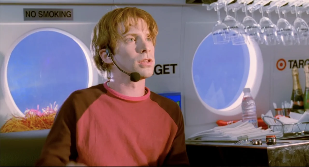 Josie and the Pussycats (2001) movie still: medium — The interior of a brightly lit airplane cabin features circular windows and a service bar. A…